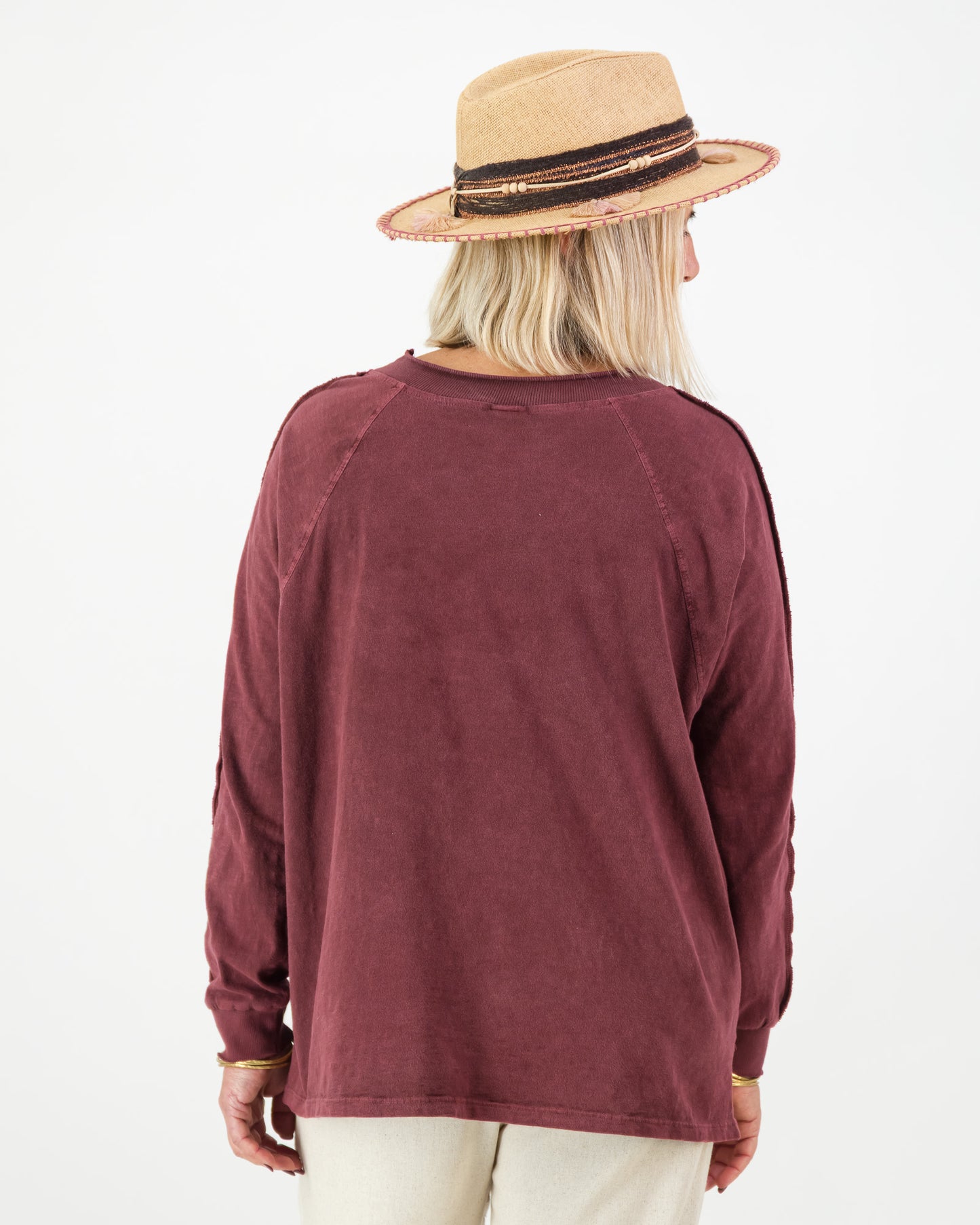Back view of a woman wearing a burgundy long sleeved cotton top and beige hat on a white background