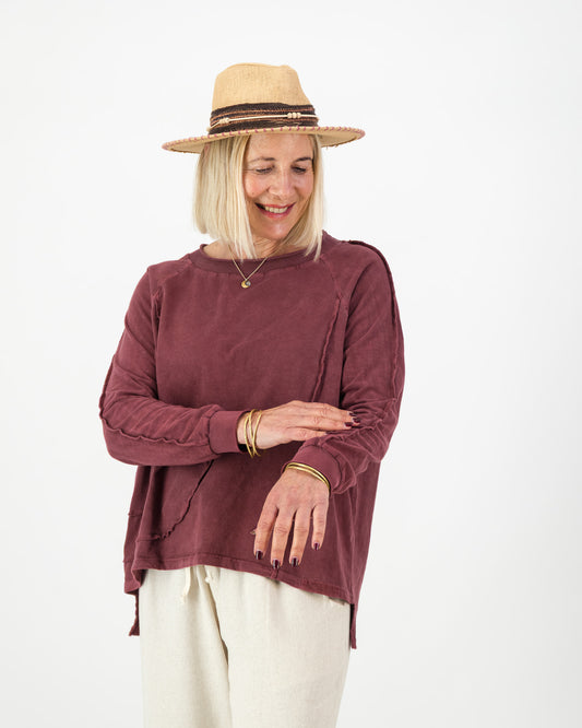 Woman wearing a burgundy long sleeved cotton top and beige hat on a white background