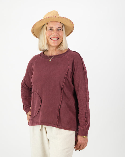 Woman wearing a burgundy long sleeved cotton top and beige hat on a white background